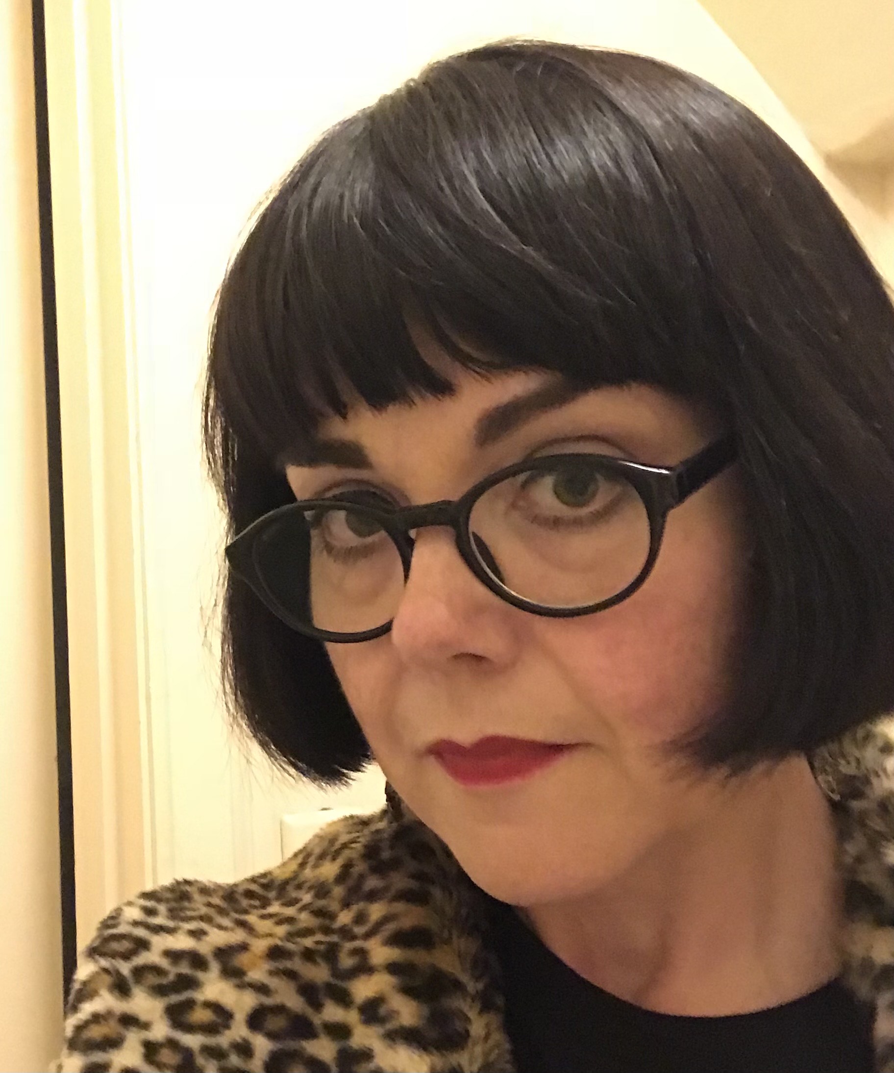 Amyellen Kessler, a woman with a dark bob haircut, wearing dark black framed glasses, a leopard-print jacket over a black shirt.